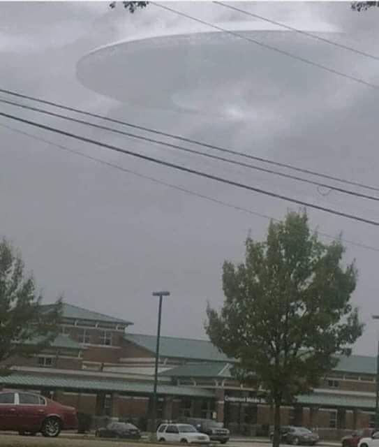 A huge saucer shaped UFO/UAP seen hovering and hiding in the clouds over an urban area. 