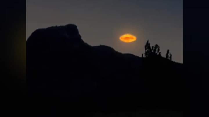 A saucer shaped UFO with glowing energy toroid hovering over a ridge in the desert. 