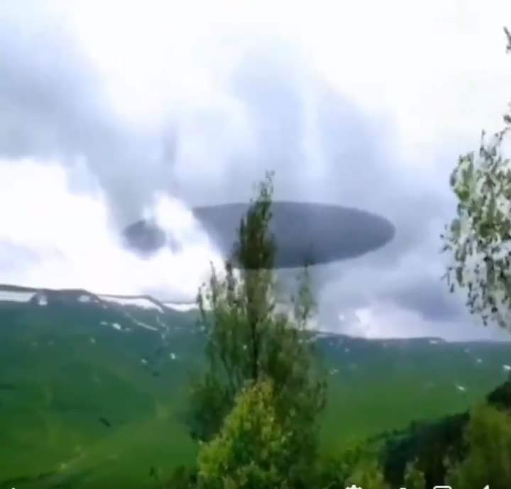 An image of a huge saucer shaped UFO emerging from the clouds. 